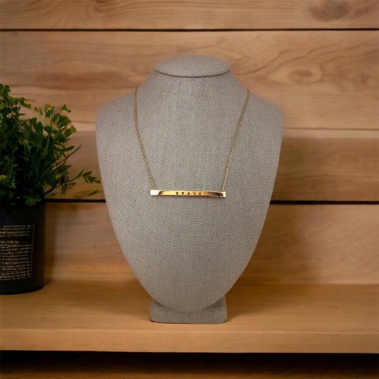 Gold necklace with 'Brave' inscribed bar