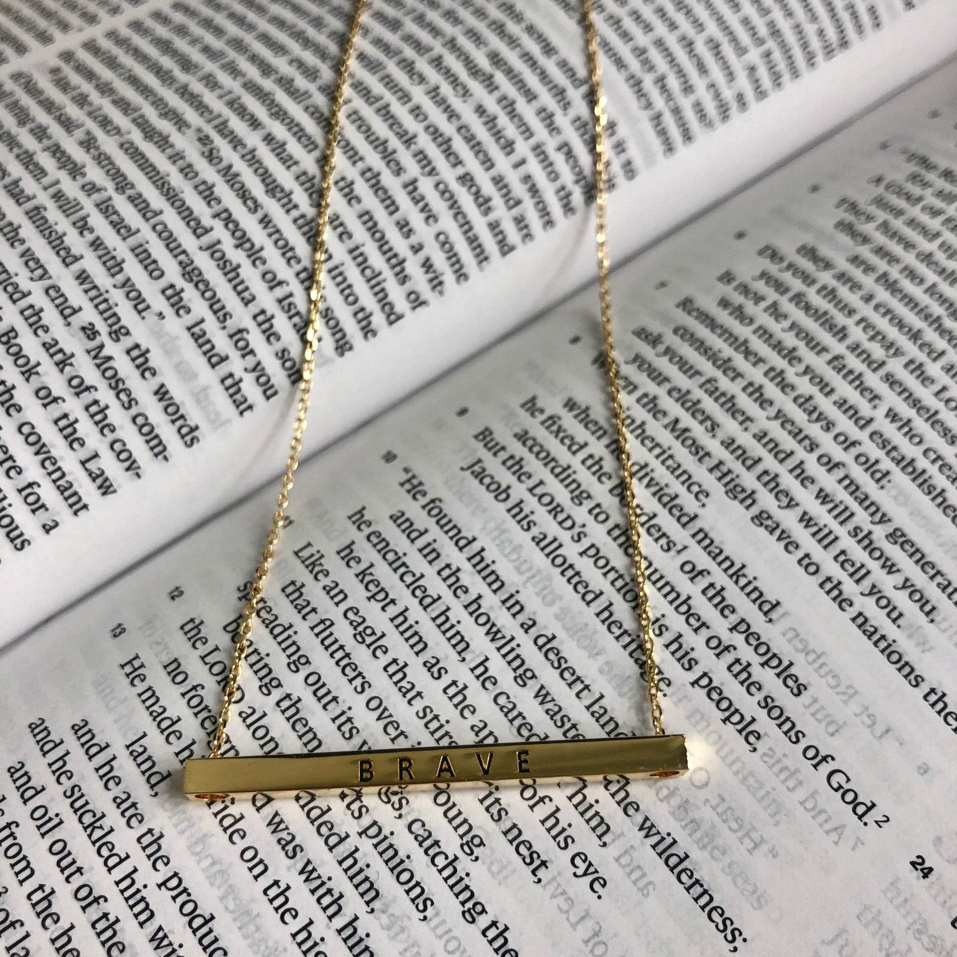 A gold bar necklace with the word "Brave" engraved on it