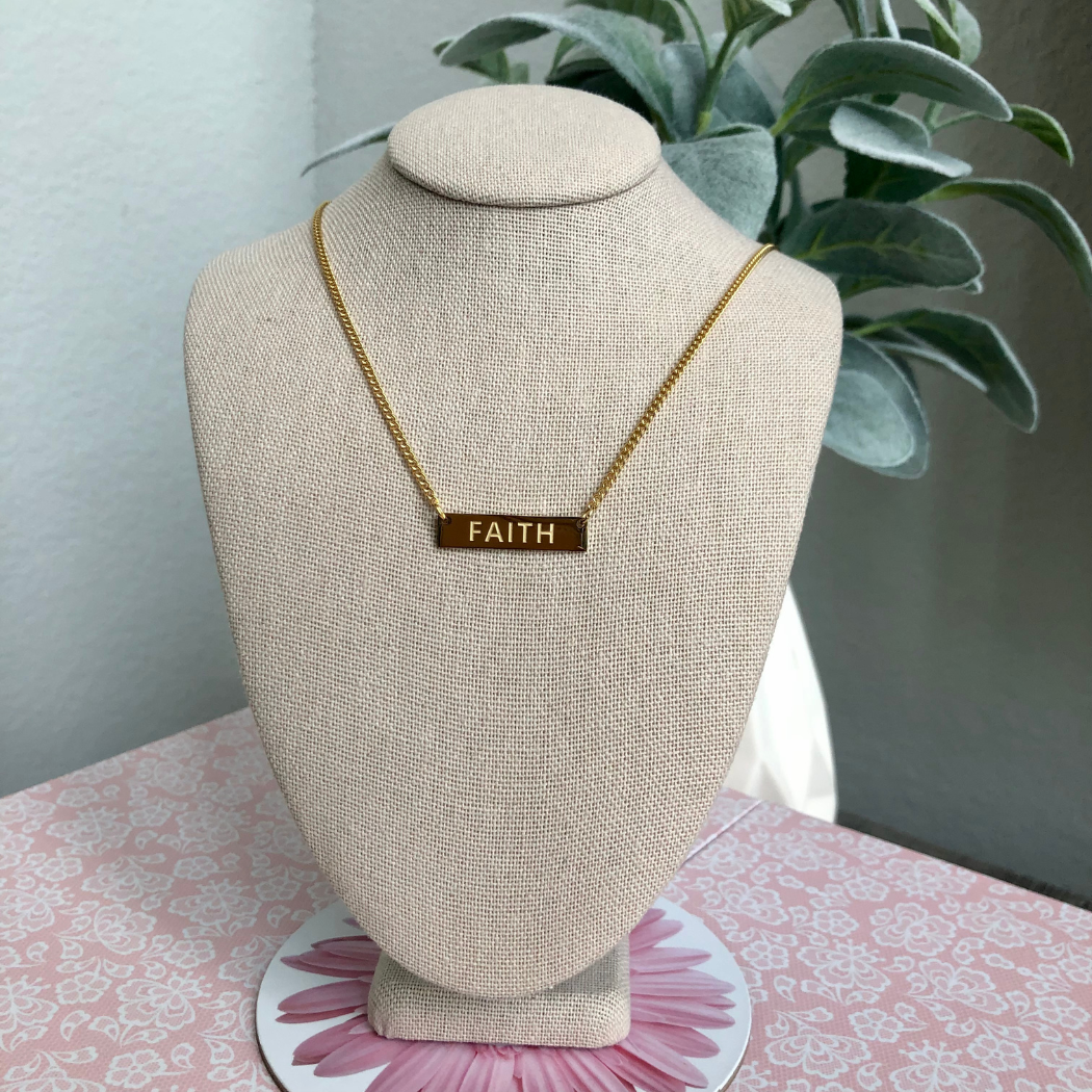 Gold necklace with the word Faith engraved.
