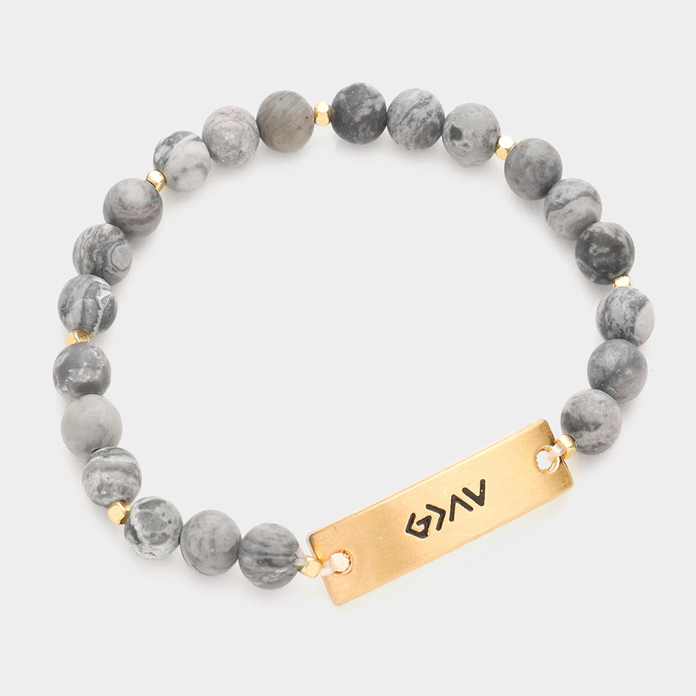 A natural stone bracelet with a metal bar featuring the engraved phrase "God is Greater Than the Highs and Lows."